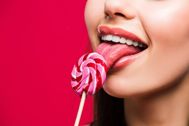 Cropped image of woman licking colored lollipop isolated on red