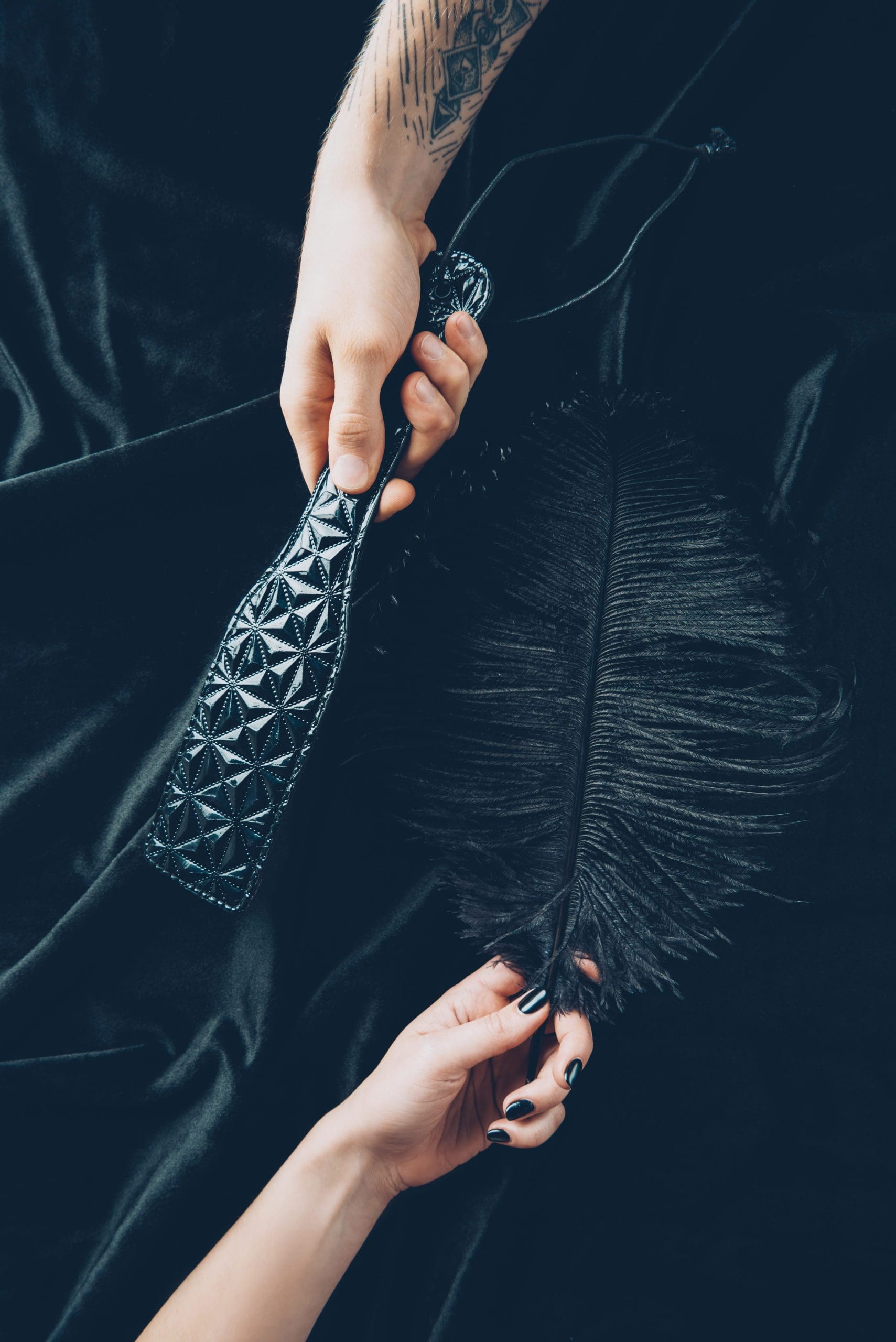 cropped shot of couple holding black feather and leather spanking paddle