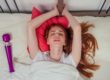 redhaired ginger female person lying on a bed with pink pillows eyes closed from pleasure next to the purple vibrator
