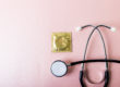Directly above shot of stethoscope with condom in pack against pink background, copy space. medical, test, std, aids, sexual, contraception, protection and healthcare concept.