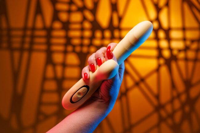 A soft female hand with a striking red manicure firmly holds a dildo